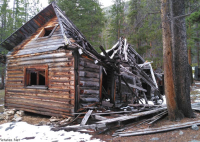 June picture of a log cabin with a collapsed roof in the Coolidge Ghost town. Image is from the Coolidge Montana Picture Tour.
